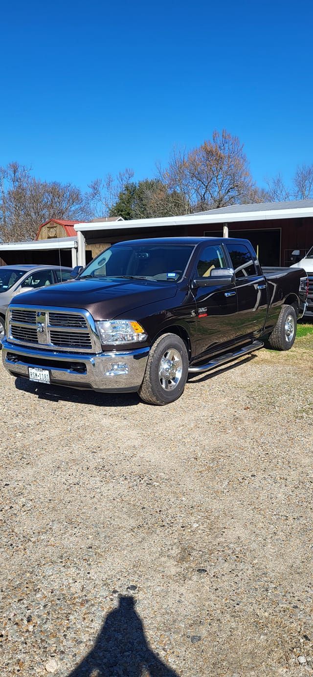 Dark brown Ram pickup truck on a gravel lot under a blue sky. Shadow in the foreground.