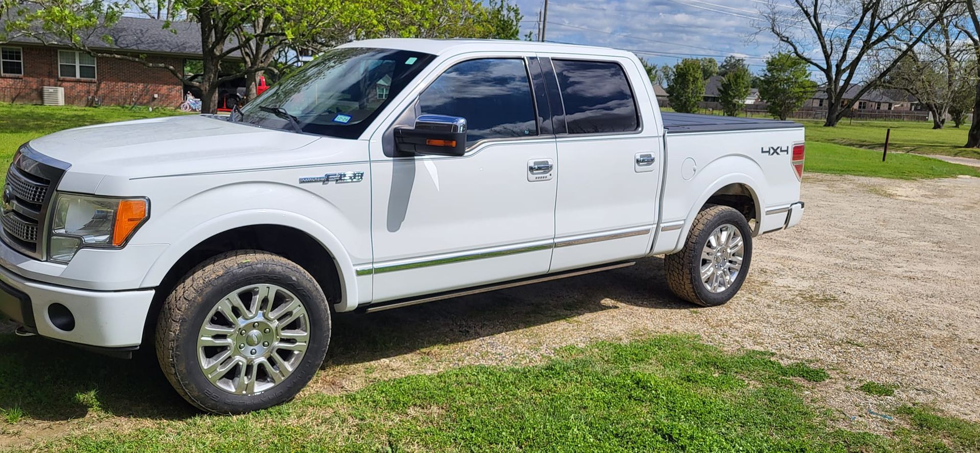 White Ford F-150 truck parked on grass and gravel. 