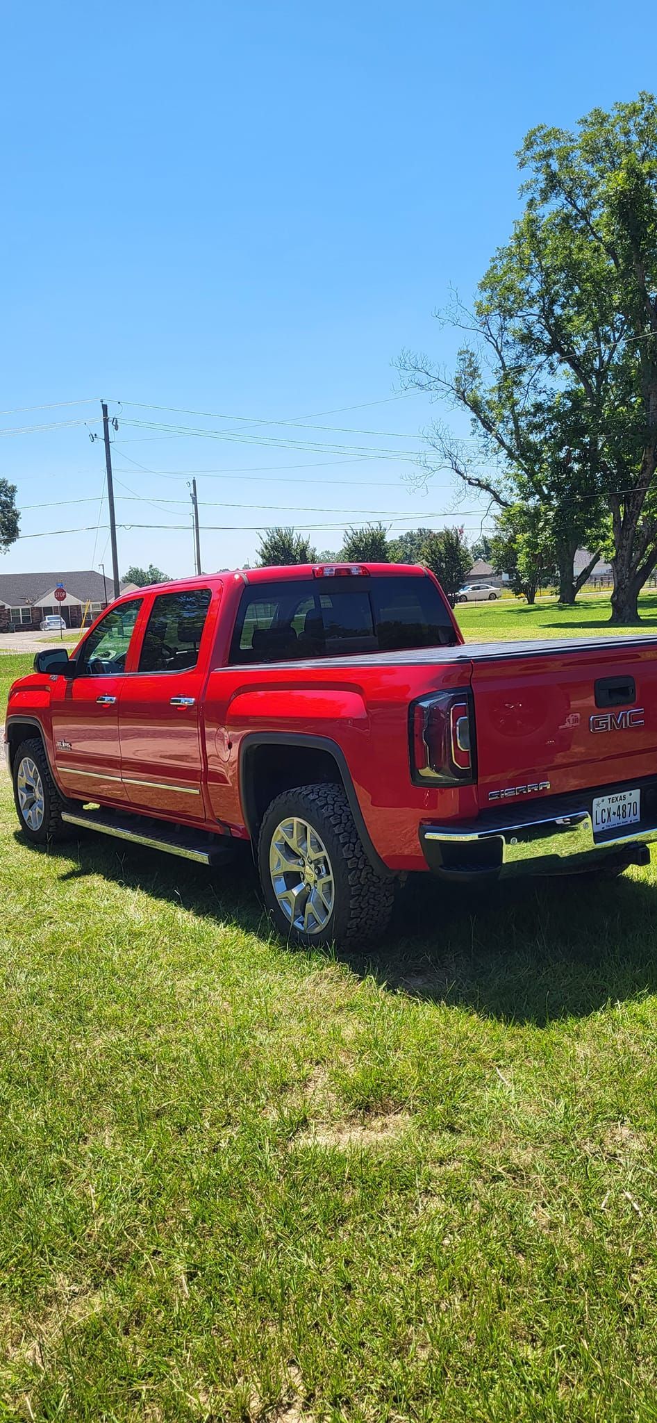 Red GMC truck parked on a grassy area under a bright blue sky.