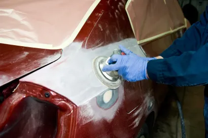 Person in blue gloves sanding car body with a power sander during auto repair.