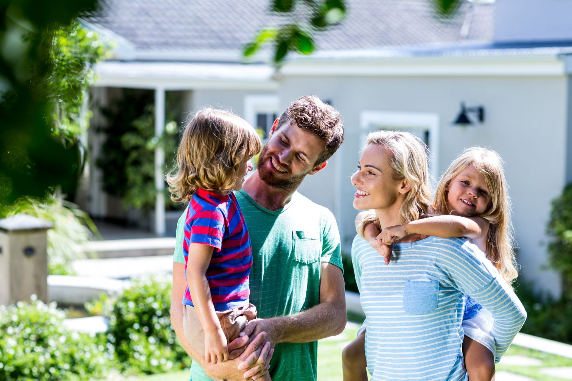 Four people smiling together in a sunny backyard in front of a house