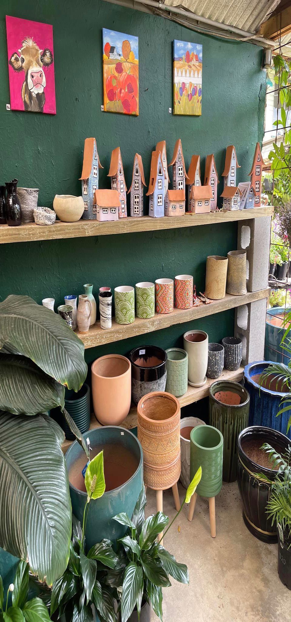 Shelves with pottery and paintings in a garden shop, with green and neutral tones.