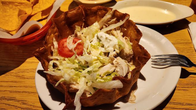 A white plate topped with a taco salad and a fork on a wooden table.