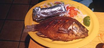 A yellow plate topped with a fish and a baked potato