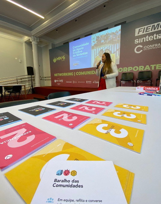 Uma mulher está fazendo uma apresentação em frente a uma tela grande em uma sala de conferências.