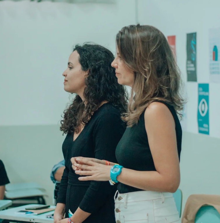 Duas mulheres estão de pé uma ao lado da outra em uma sala com pôsteres na parede