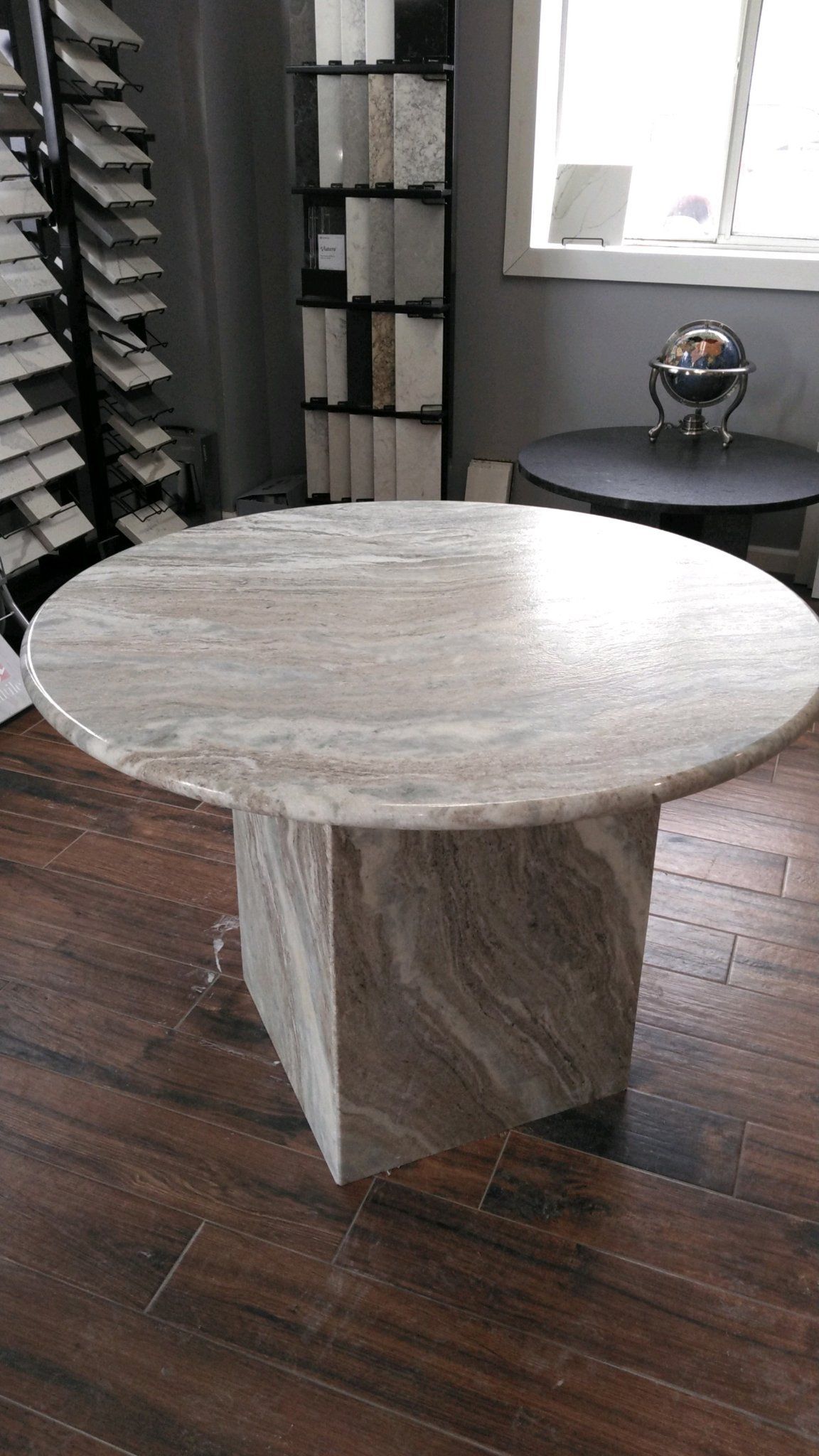 A round marble table is sitting on a wooden floor in a room - Luther Falls Kitchen & Bath - Champaign, IL