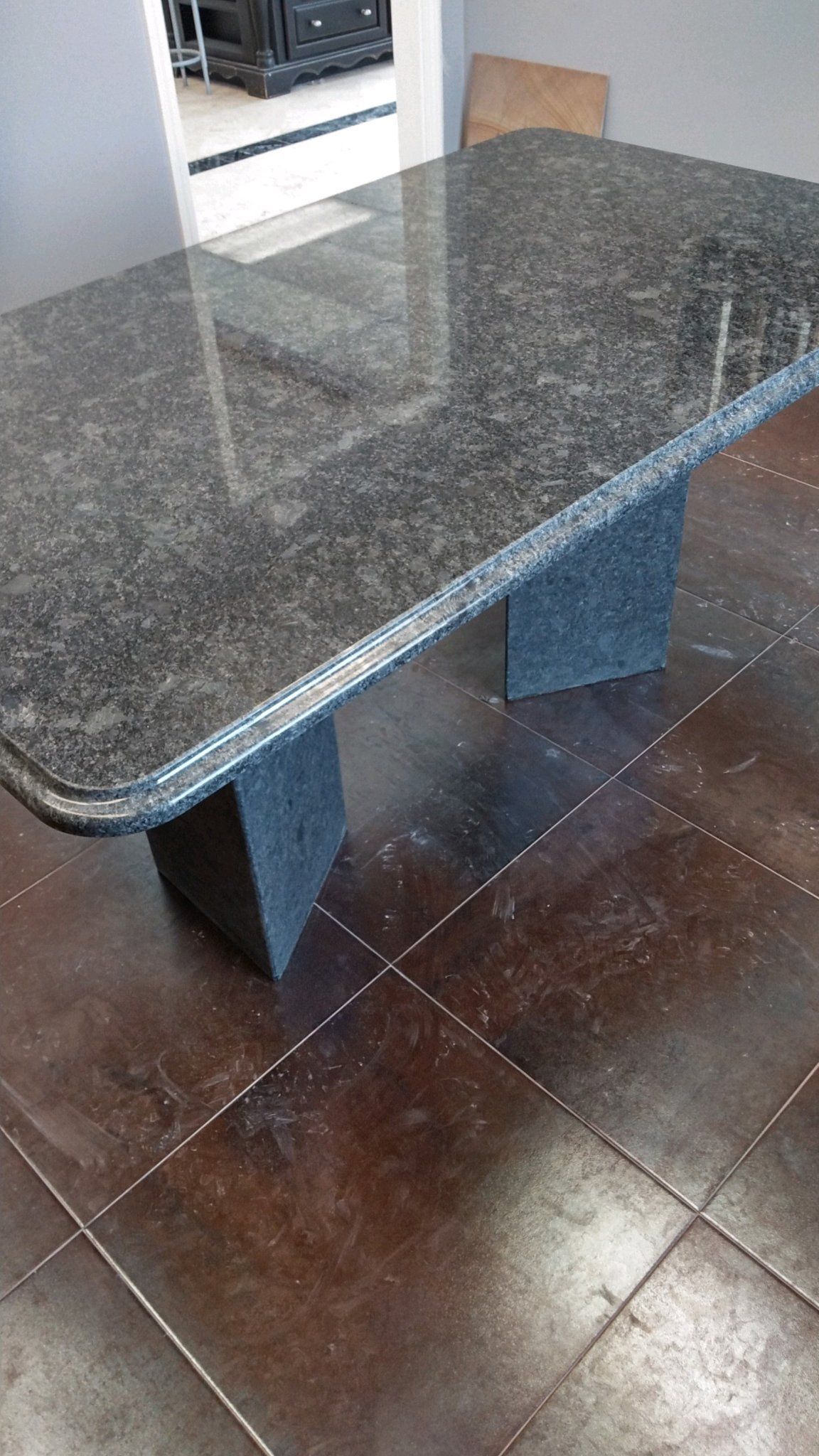A granite table is sitting on a tiled floor in a room- Luther Falls Kitchen & Bath - Champaign, IL