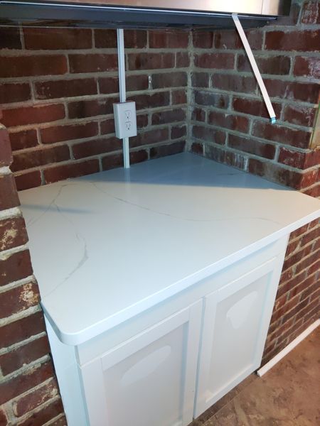 A corner of a kitchen with a white counter top and a brick wall - Luther Falls Kitchen & Bath - Champaign, IL