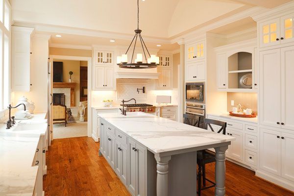 A modern kitchen with white cabinets, a large marble island, and stainless steel appliances.