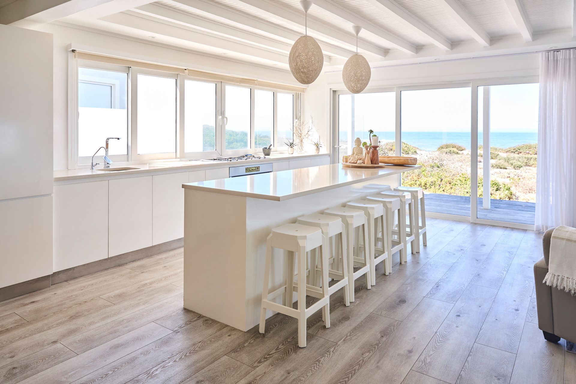 A kitchen remodeling project with an island, white cabinets, quartz counter and ocean views behind.