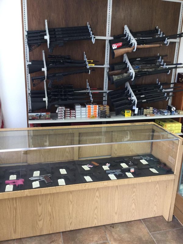 Display of handguns and knives in a shop case and wall rack, with ammunition boxes below.