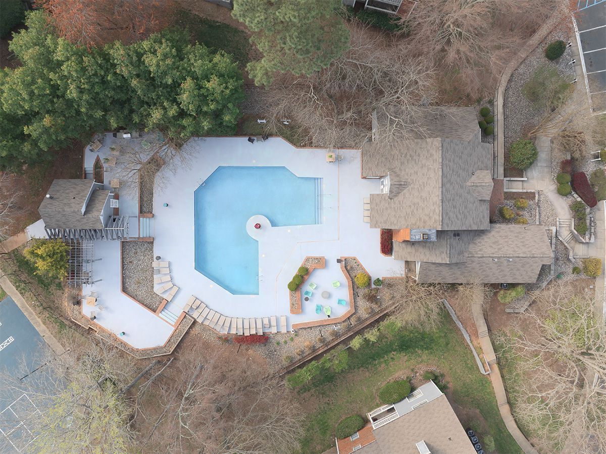 Overhead view of a house with a swimming pool. Gray roof and patio surround the light blue pool.
