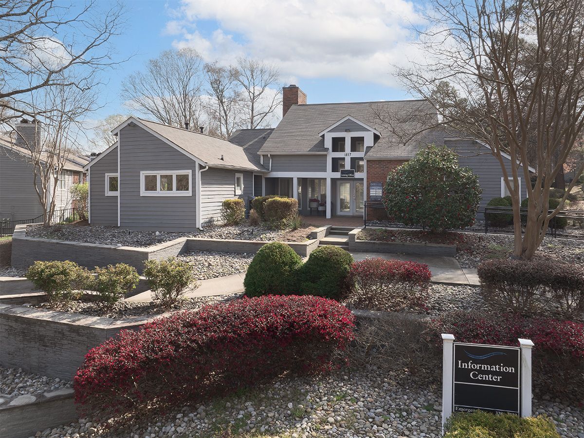 Gray building with a brick chimney and landscaping, a sign reads