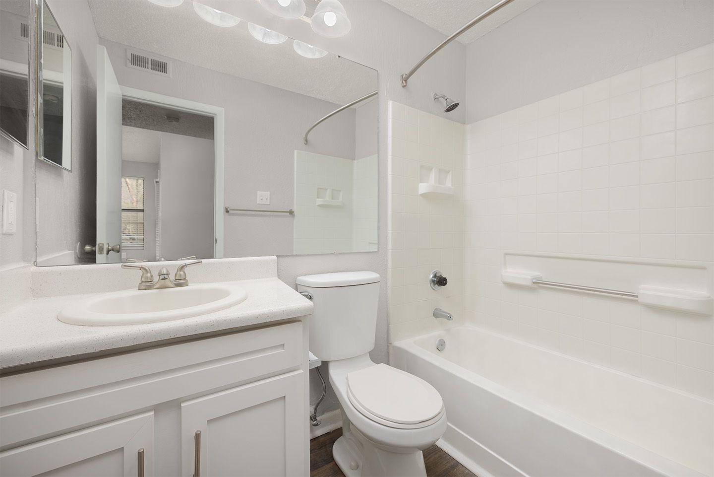 White bathroom with a toilet, sink, bathtub, and large mirror.