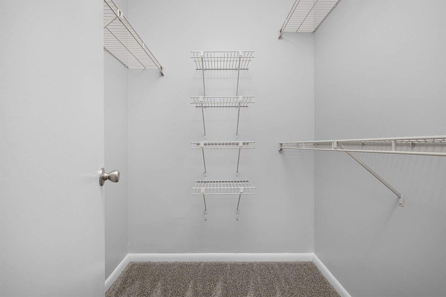 Empty walk-in closet with white wire shelving and a gray carpet.