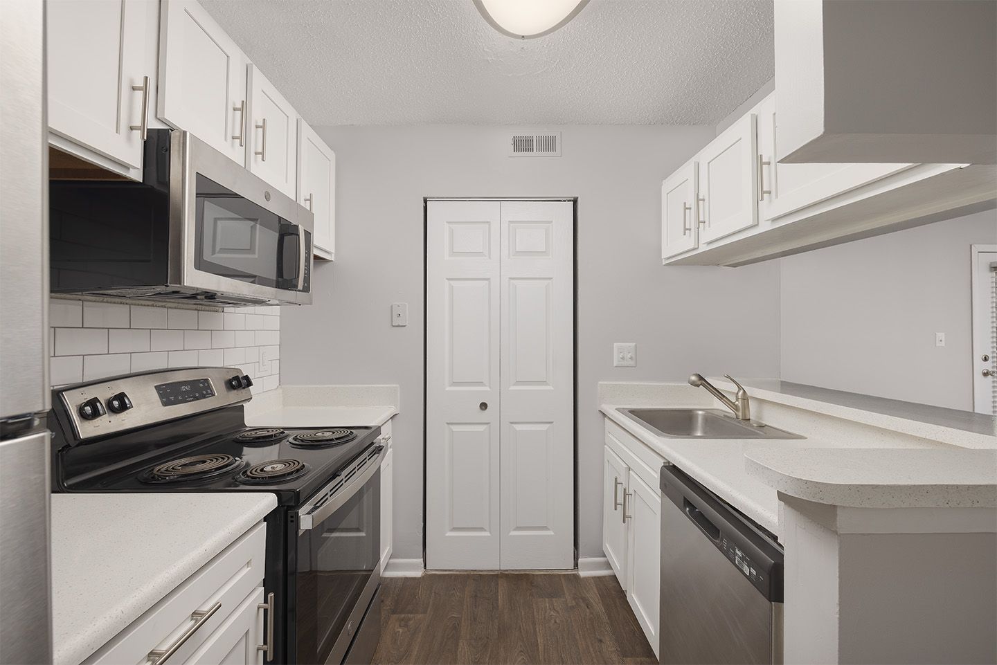 White kitchen with stainless steel appliances and white cabinets, wooden floors.