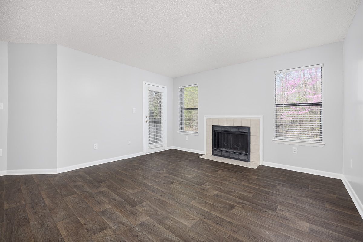 Empty room with dark wood floors, white walls, fireplace, and windows.