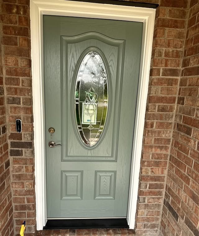 A door with an oval window is on a brick wall.