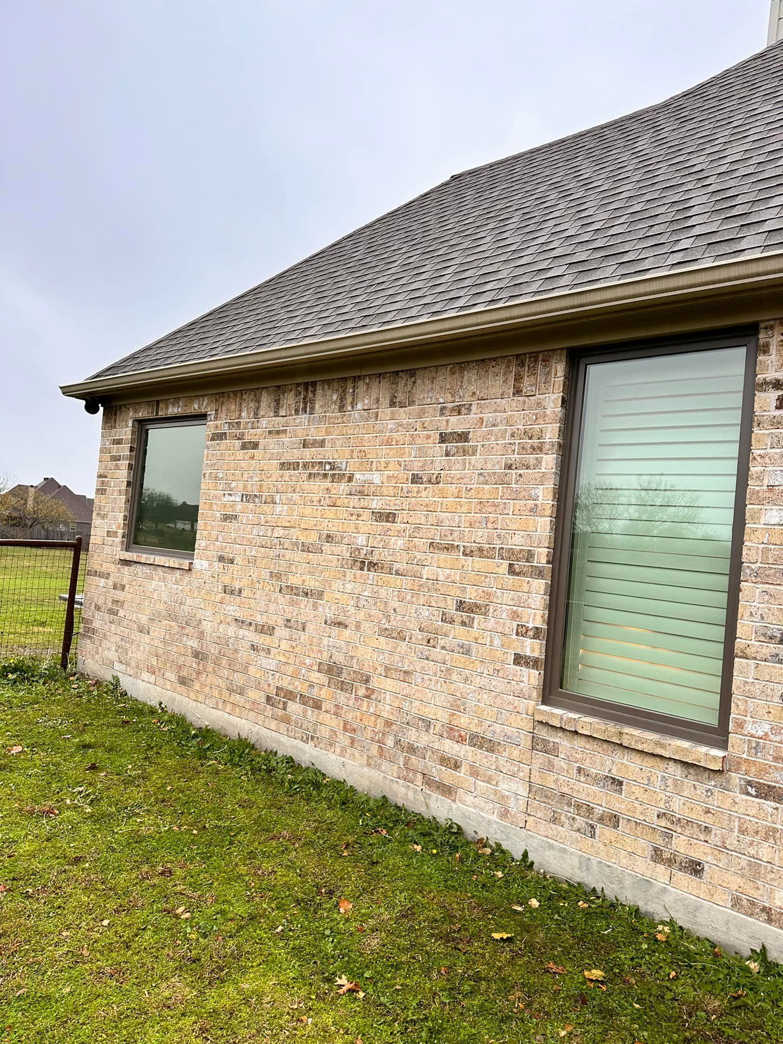 A brick house with two windows and a roof is sitting on top of a lush green field.