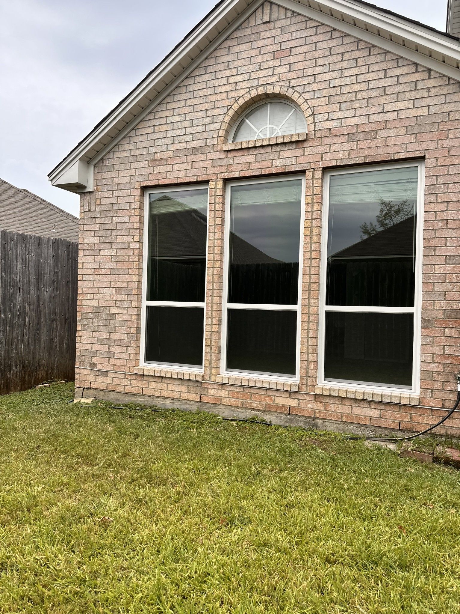 A brick house with two windows and a fence in the backyard.
