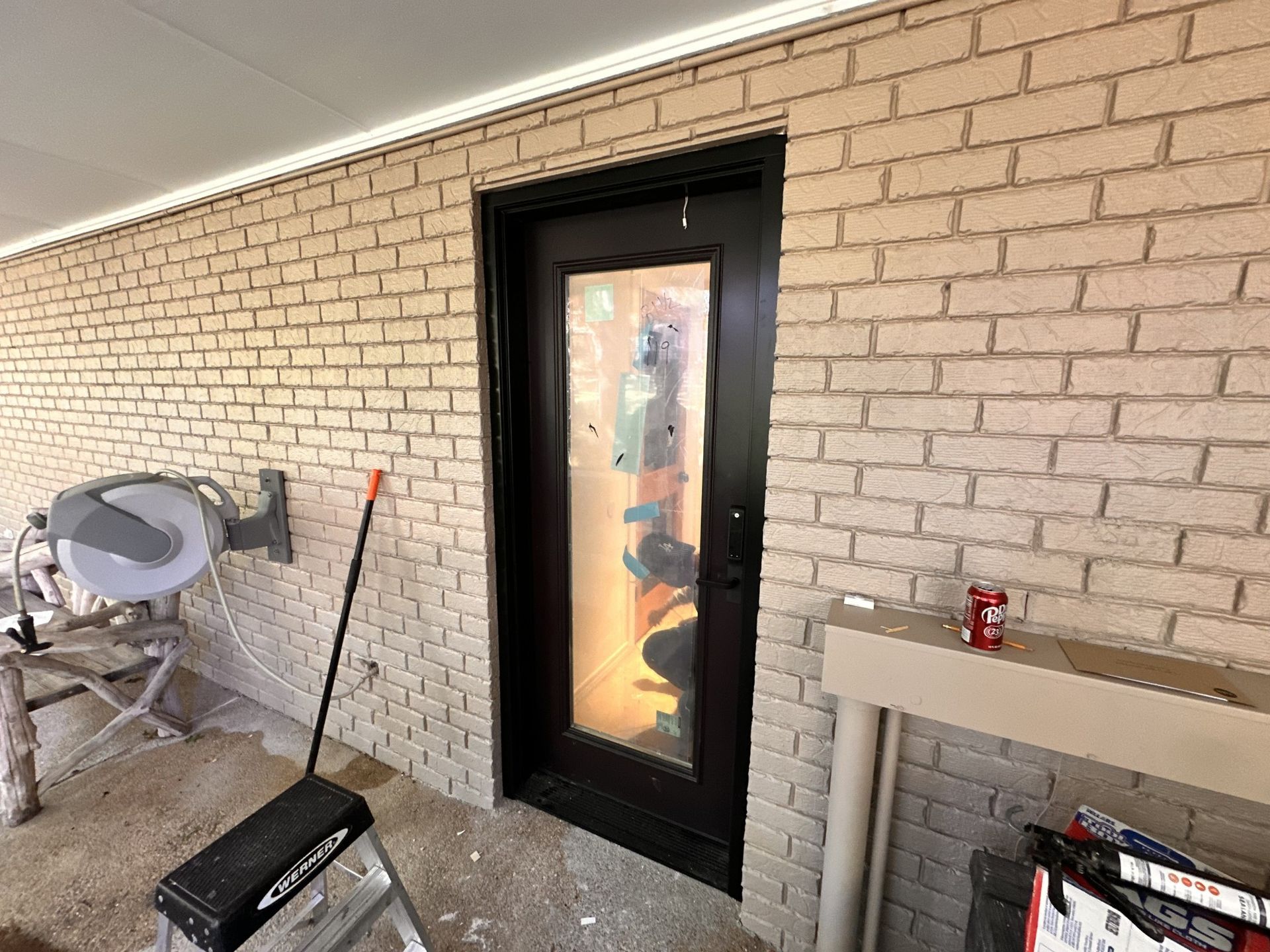 A brick wall with a black door and a ladder.