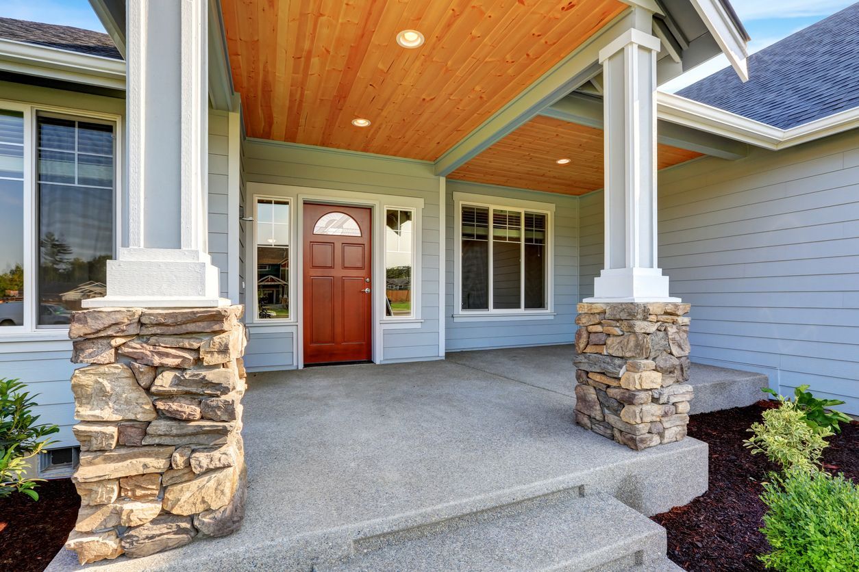 The front porch of a house with a wooden ceiling and stone pillars.