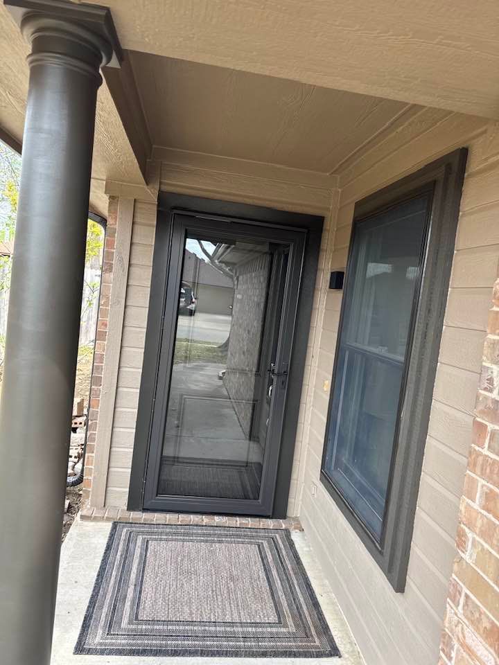 The front door of a house with a screen door and two windows.
