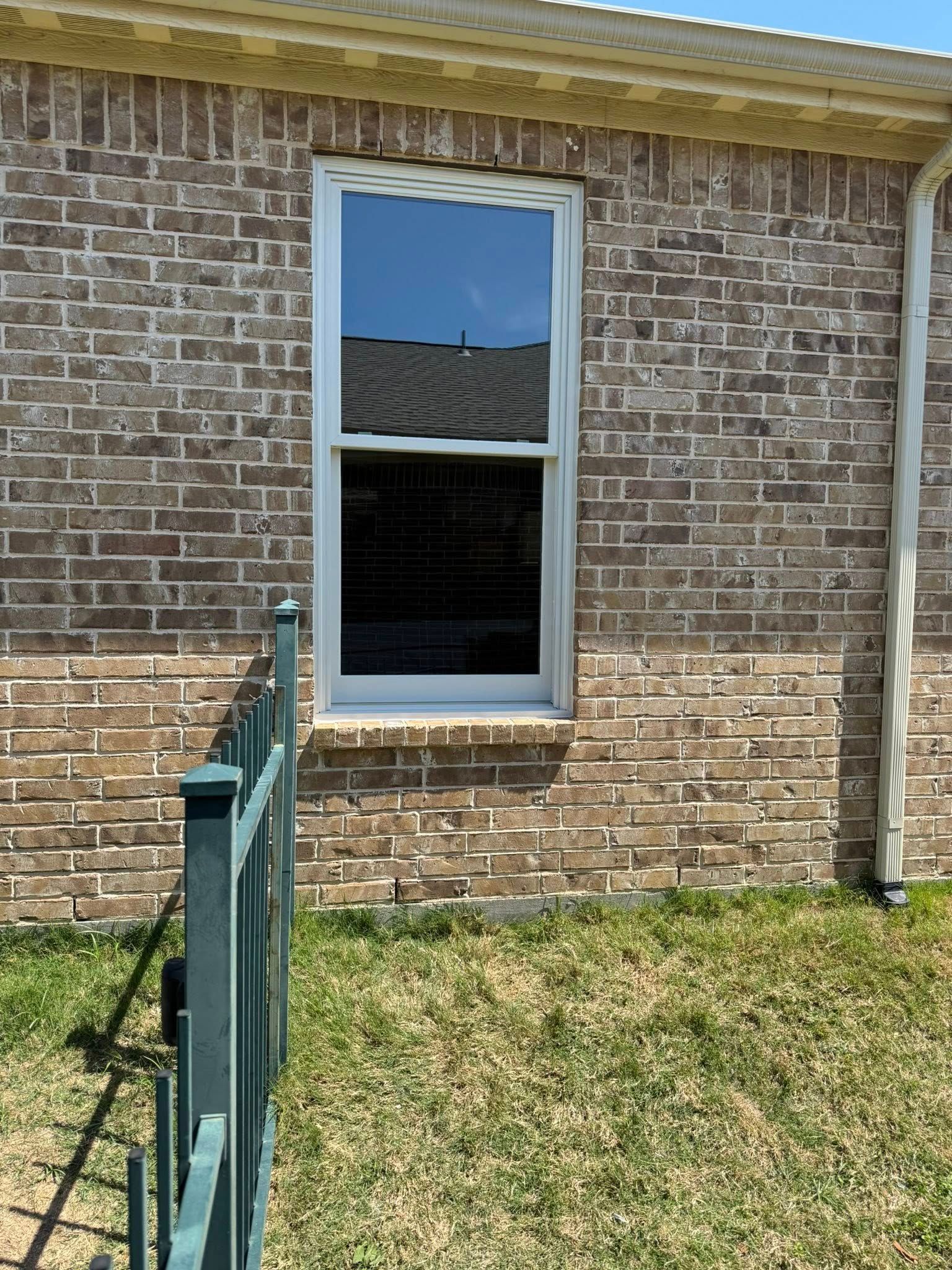 A brick house with a window and a fence in front of it.