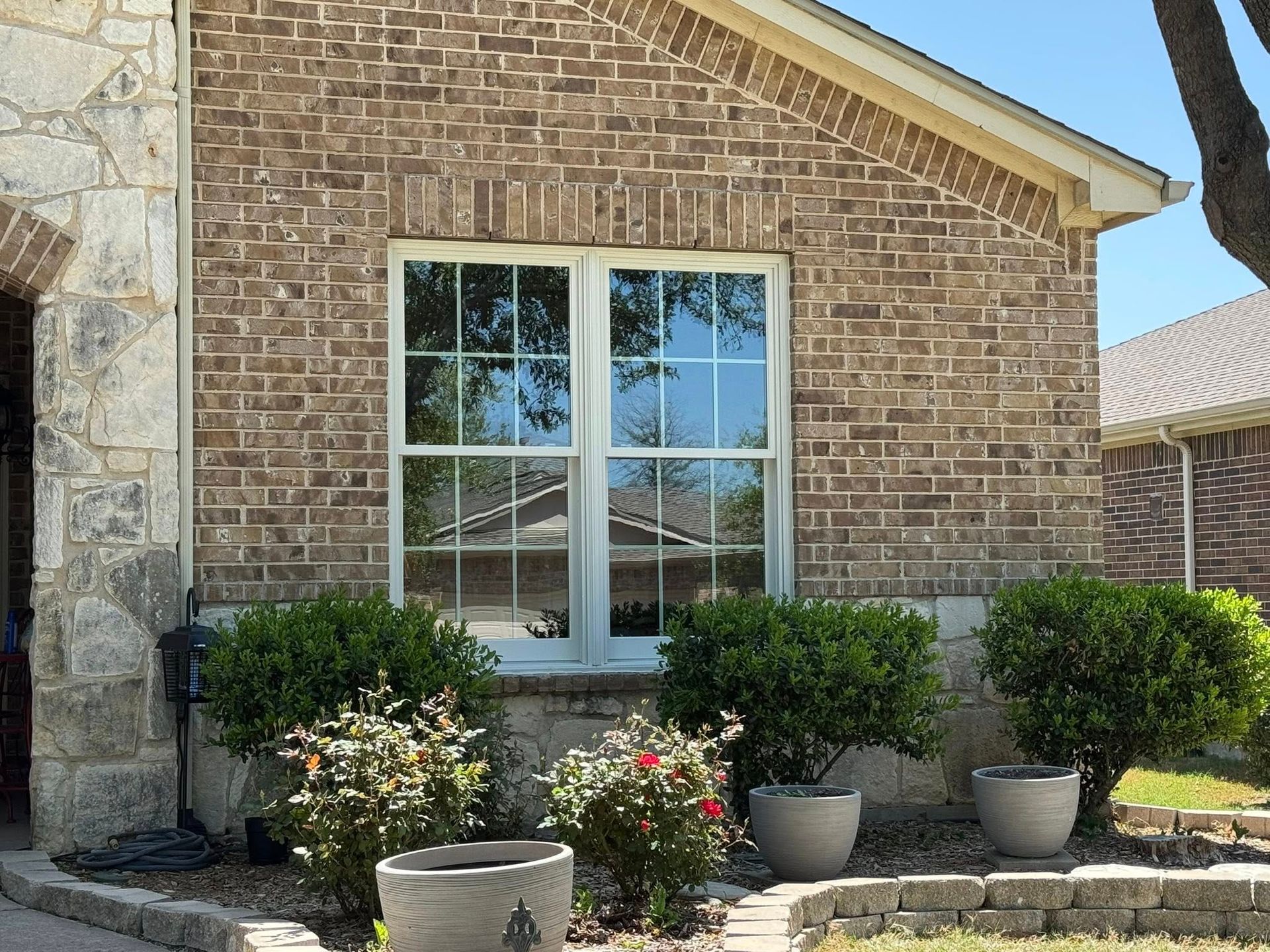 A brick house with a white window and potted plants in front of it.