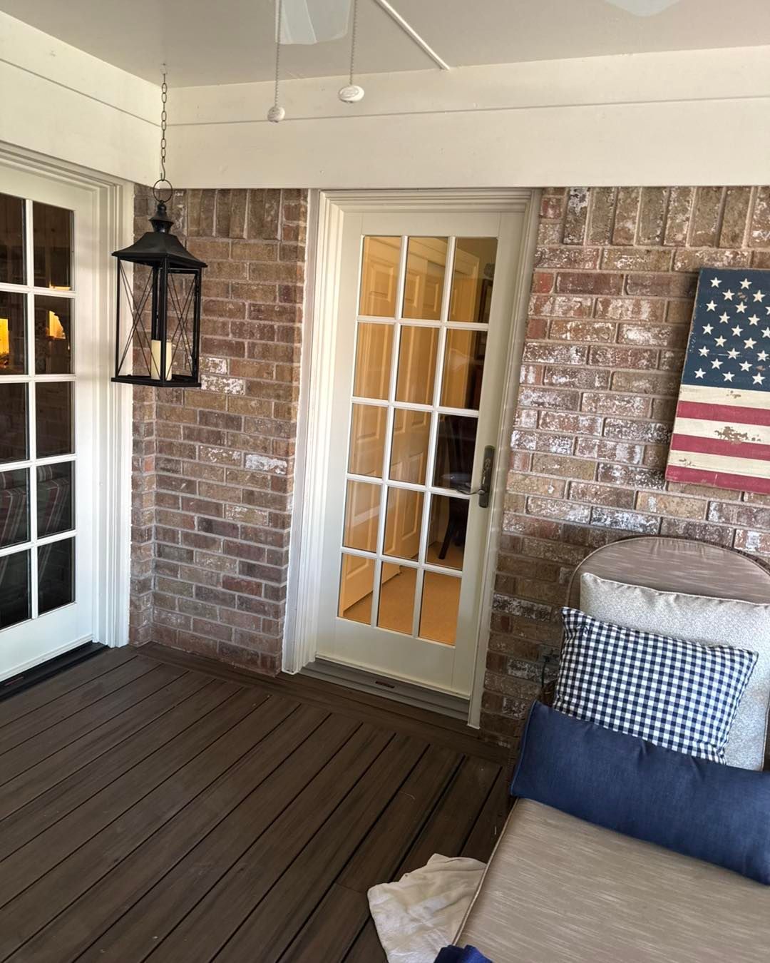 A porch with a brick wall and a lantern hanging from the ceiling.