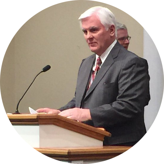 A man in a suit standing at a wooden podium and speaking into a microphone.