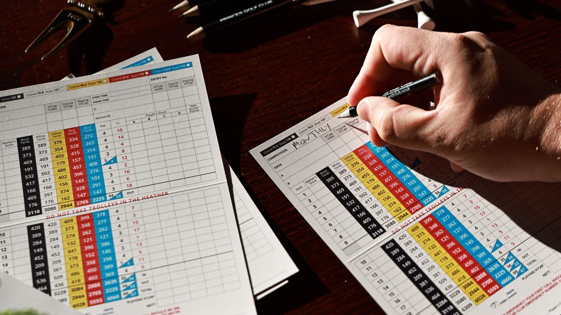 Golfer recording scores on a golf scorecard after a round, tracking performance for handicap calculation.
