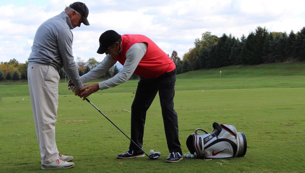 PGA professional correcting golf grip technique during one-on-one golf instruction on the driving range.