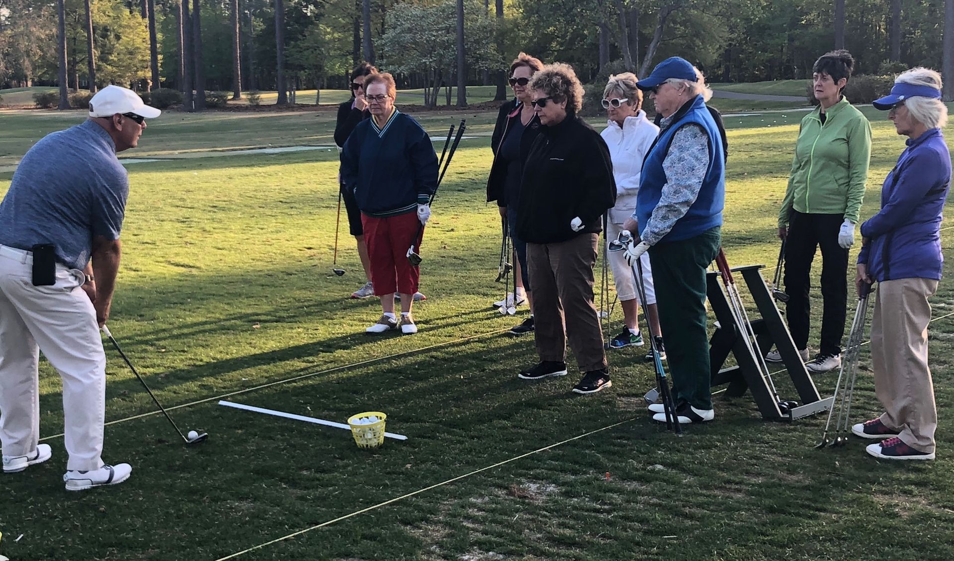 PGA golf instructor leading a group golf lesson on the driving range, teaching swing fundamentals.