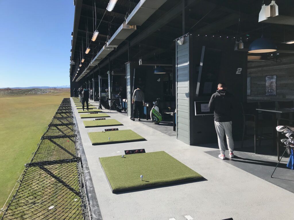 Golfers training at modern driving range with ball-tracking technology – innovative golf practice facilities in 2025.