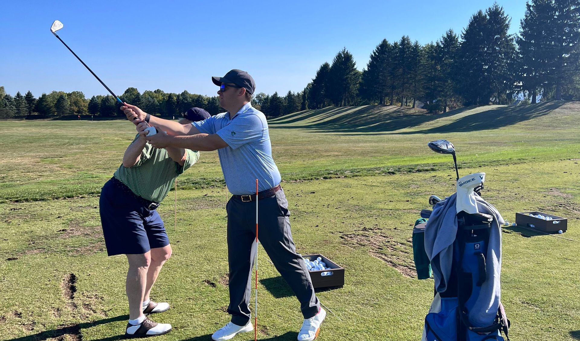 Golf instructor teaching proper swing technique on the driving range during a private golf lesson.
