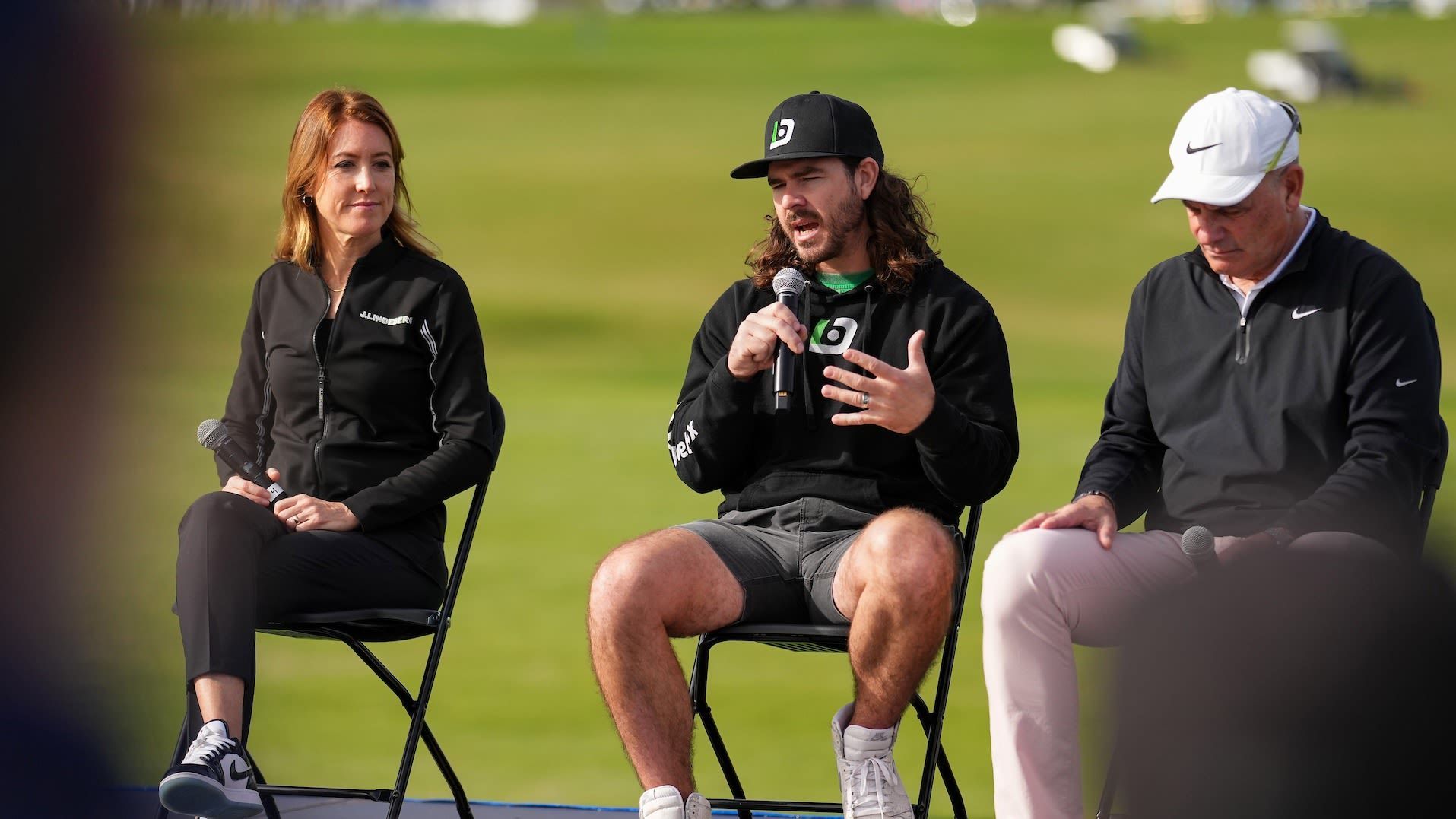 Jake Hutt, PGA, speaks and demonstrates swing techniques during PGA Show Demo Day in front of a crowd of golf professionals.
