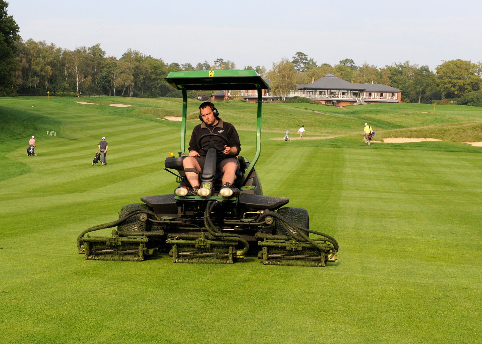 Operator cutting a fairway on a riding mower, illustrating hands-on care alongside connected turf management.