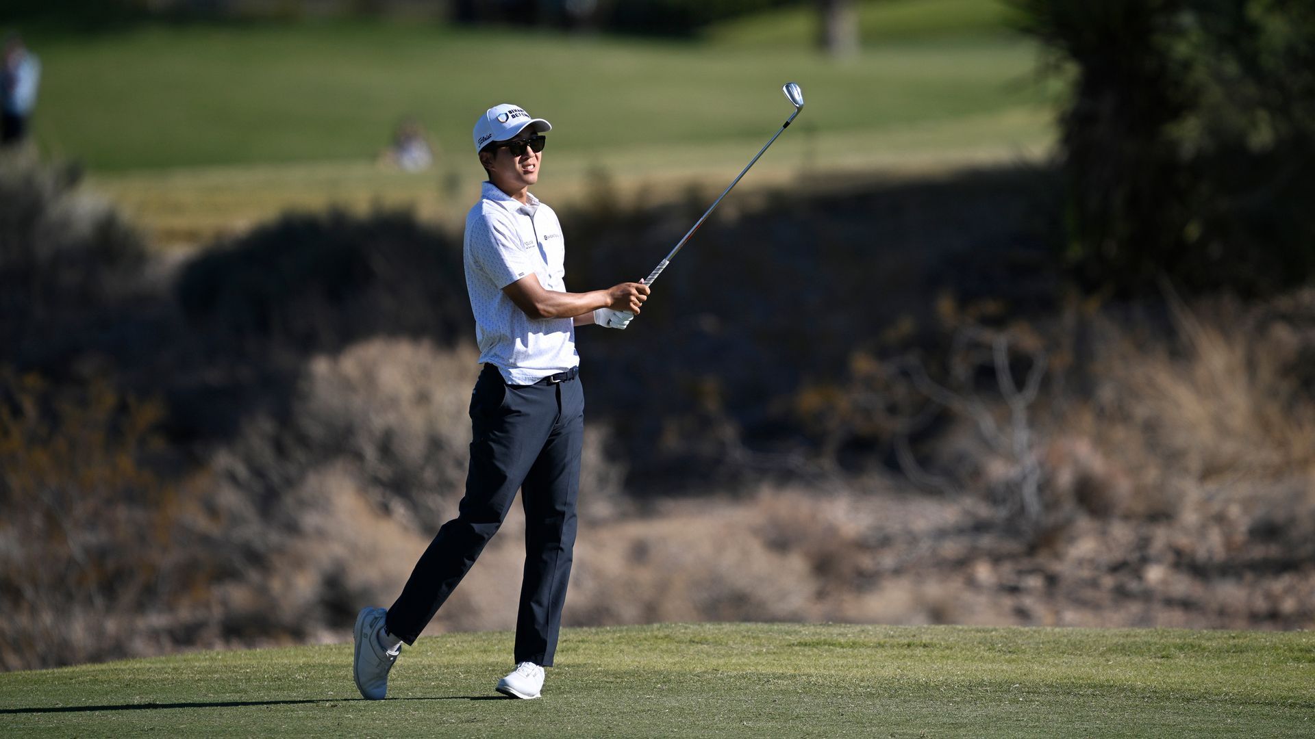 Professional golfer hitting a long iron shot with precision on the fairway.
