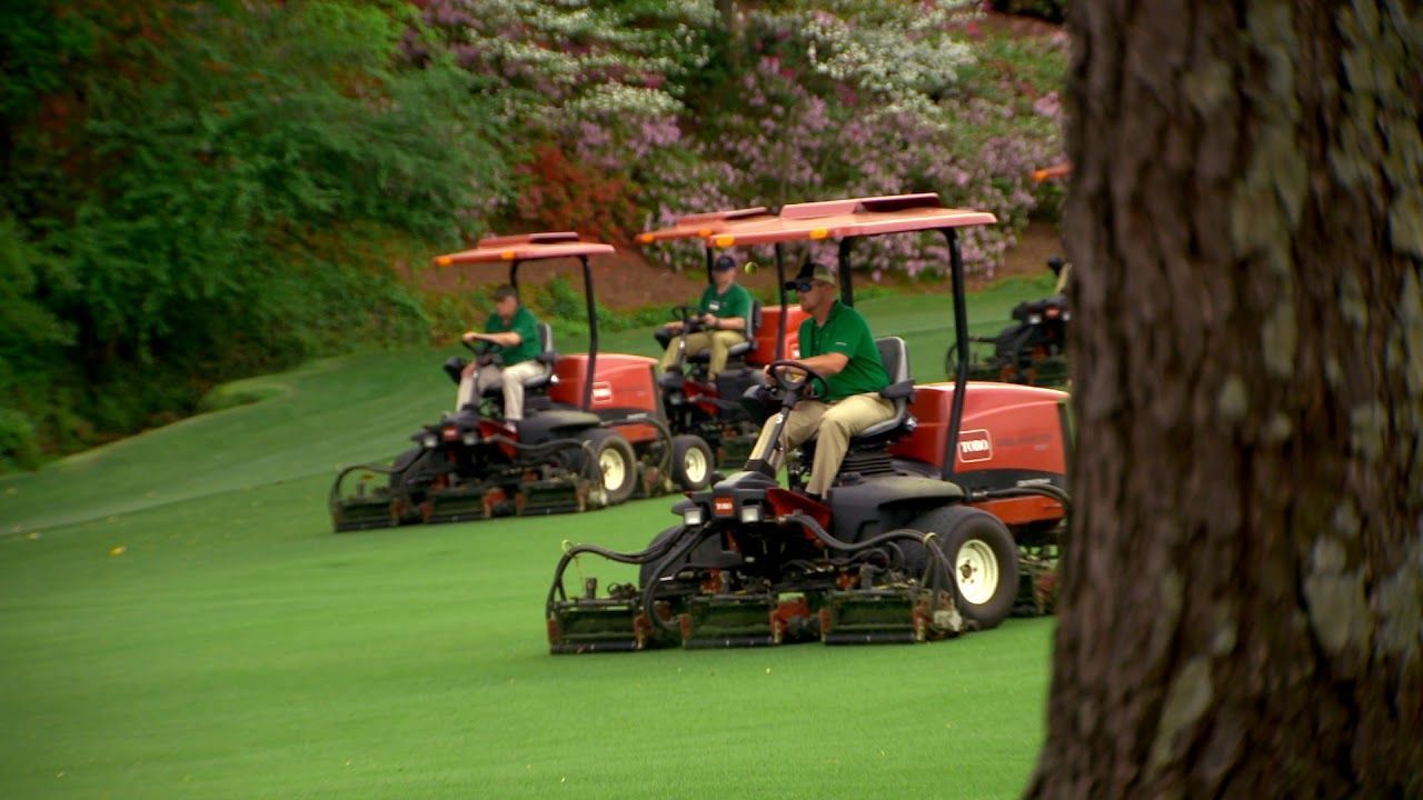 Groundskeeping team mowing the fairways at Augusta National Golf Club with precision equipment.