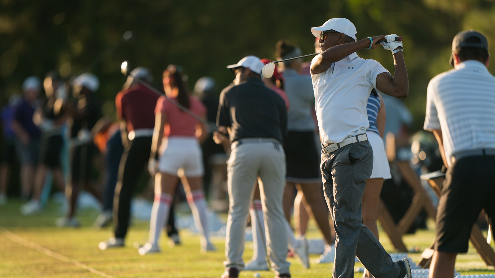 Golfers warming up on the driving range before a tournament, preparing with practice swings and focused routines.