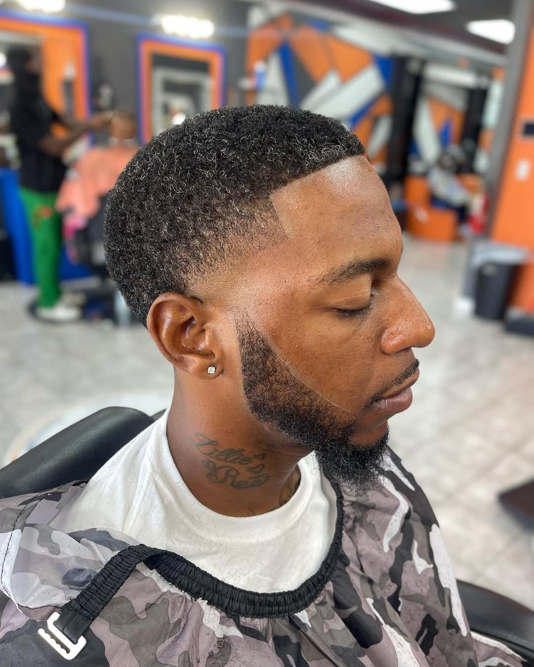 A person with a precise, faded haircut and a groomed beard sitting in a barber chair at a salon.