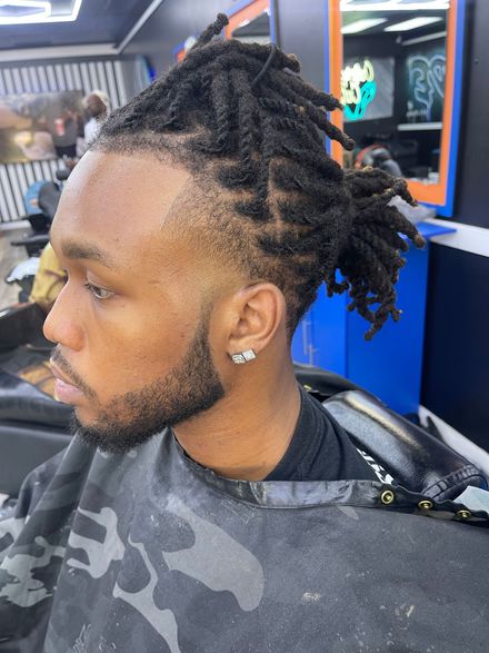 Profile view of a person with a short, buzzed hairstyle featuring an intricate, shaved tribal-inspired pattern.