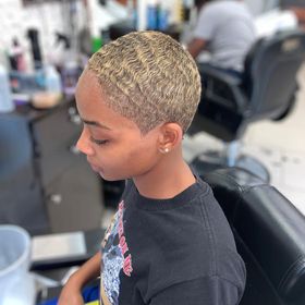 A person with short, bleached blonde hair featuring a subtle wavy texture, seated in a salon chair.