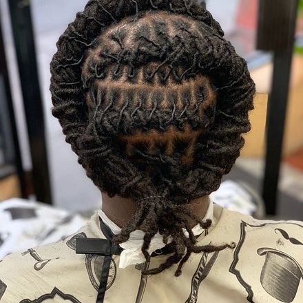 Back view of locs styled in an intricate, crisscrossing braided design with a bun and loose ends.