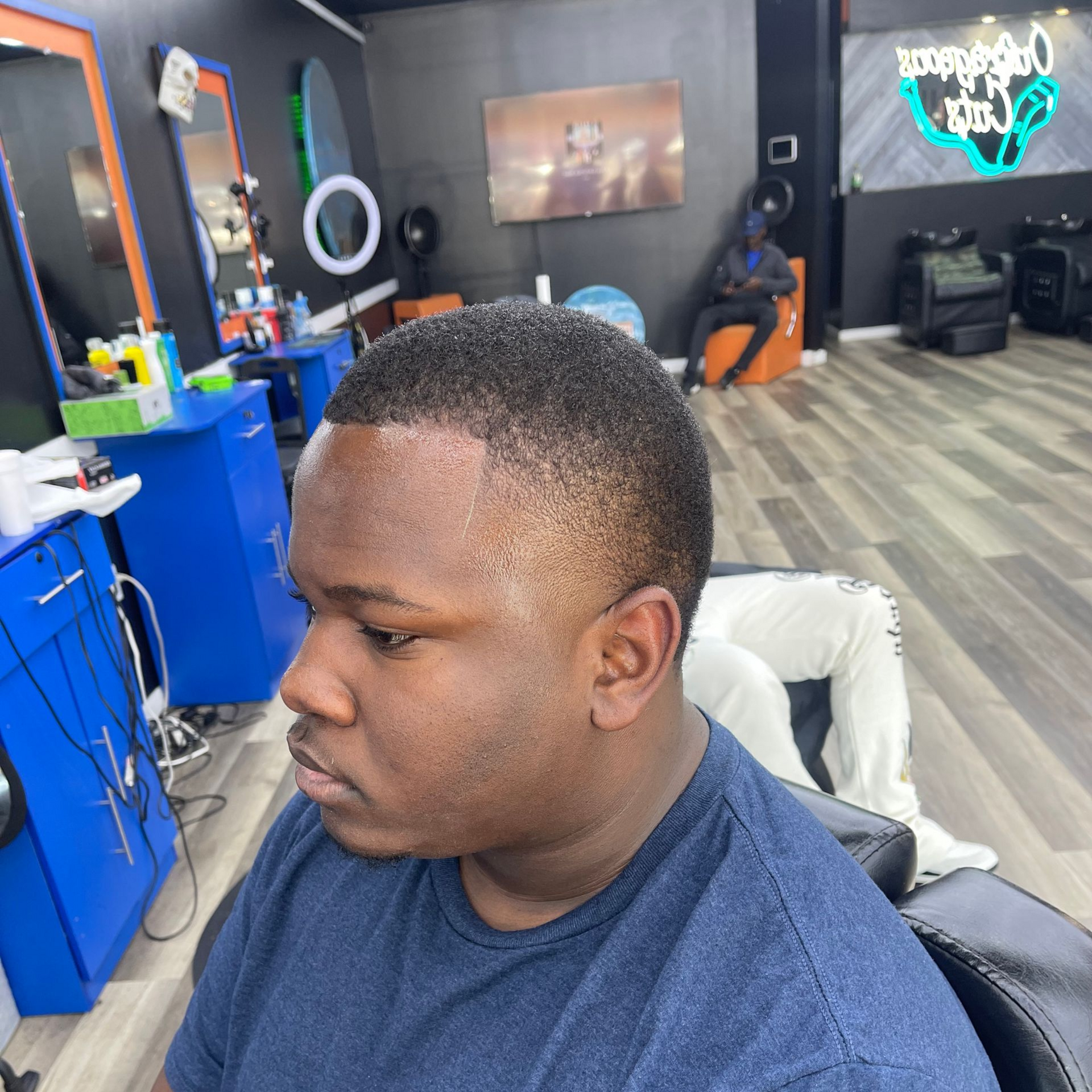 Man in a navy shirt seated in a barber shop, shown in side profile with a fresh fade haircut.