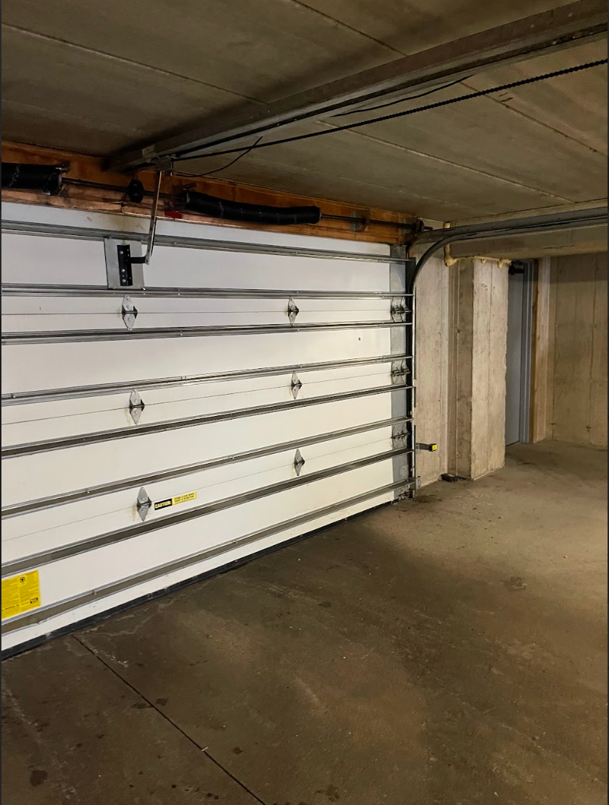 An empty garage with a white garage door open.