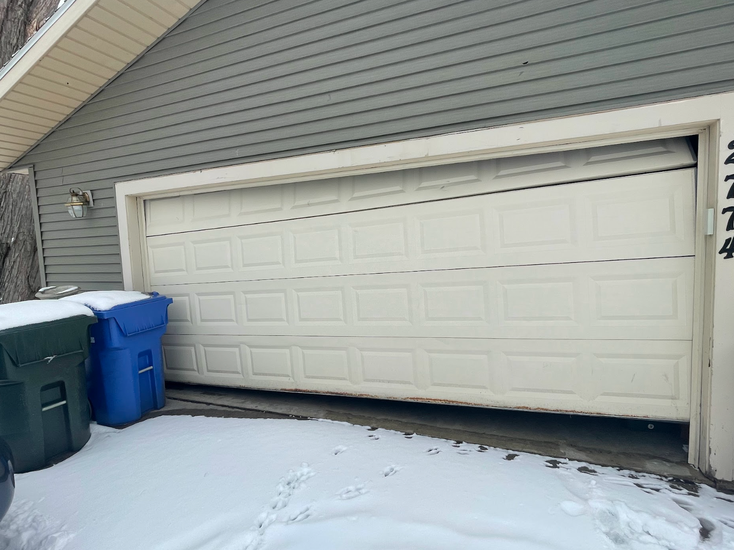 A white garage door is stuck open in the snow.