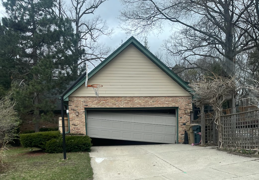 A house with a broken garage door and a basketball hoop on the roof